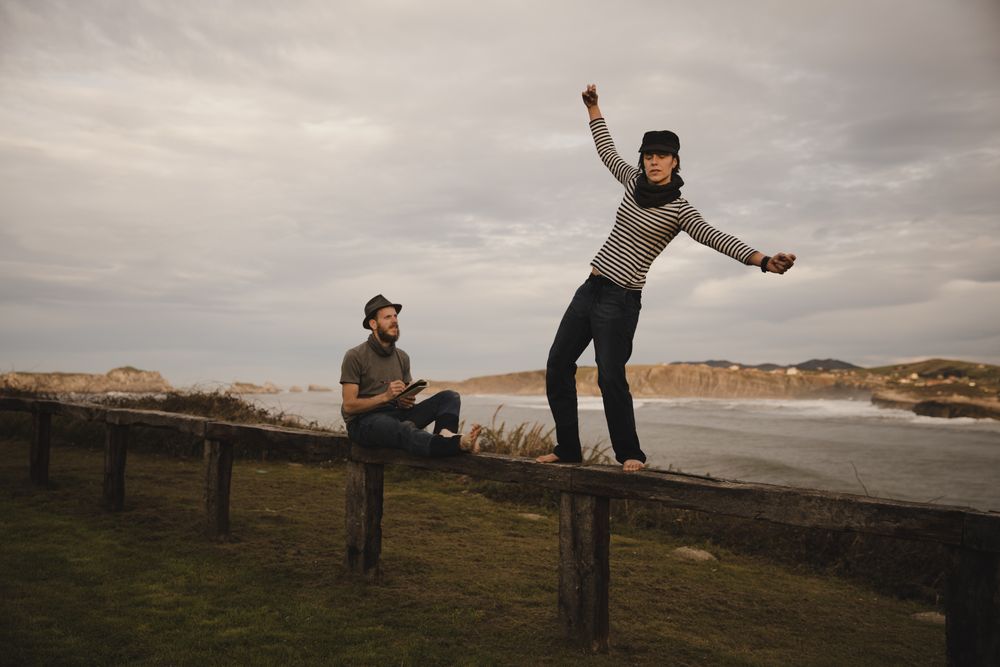 Couple holding hands and jumping on bench on shore near water