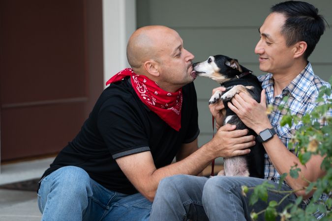 Man receiving kiss from his dog while his partner holds their dog