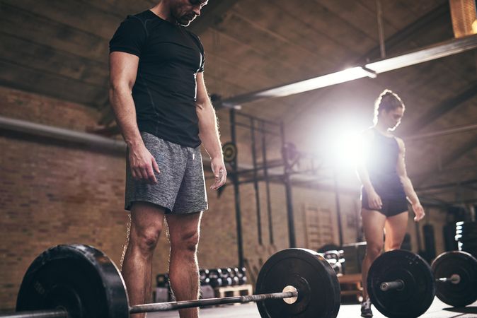 Low angle of man and woman preparing to lift barbells with weights