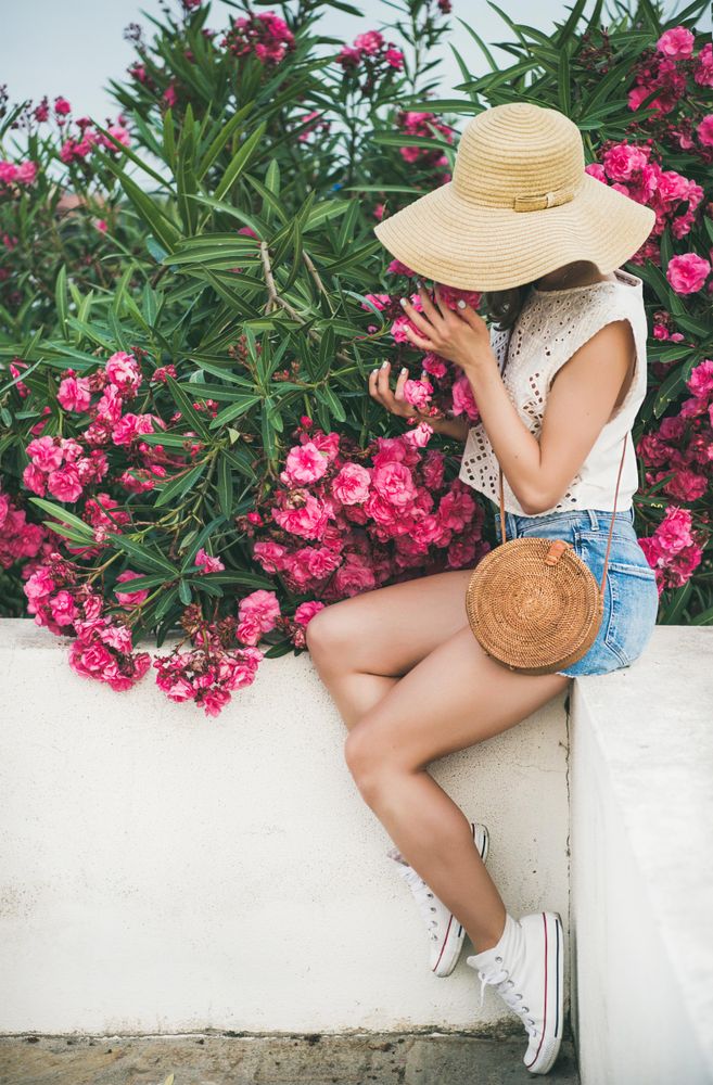 Woman sitting on white wall with pink oleander tree
