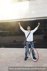 Joyful male sitting on colorful bicycle with both arms up and outstretched bxpZvb