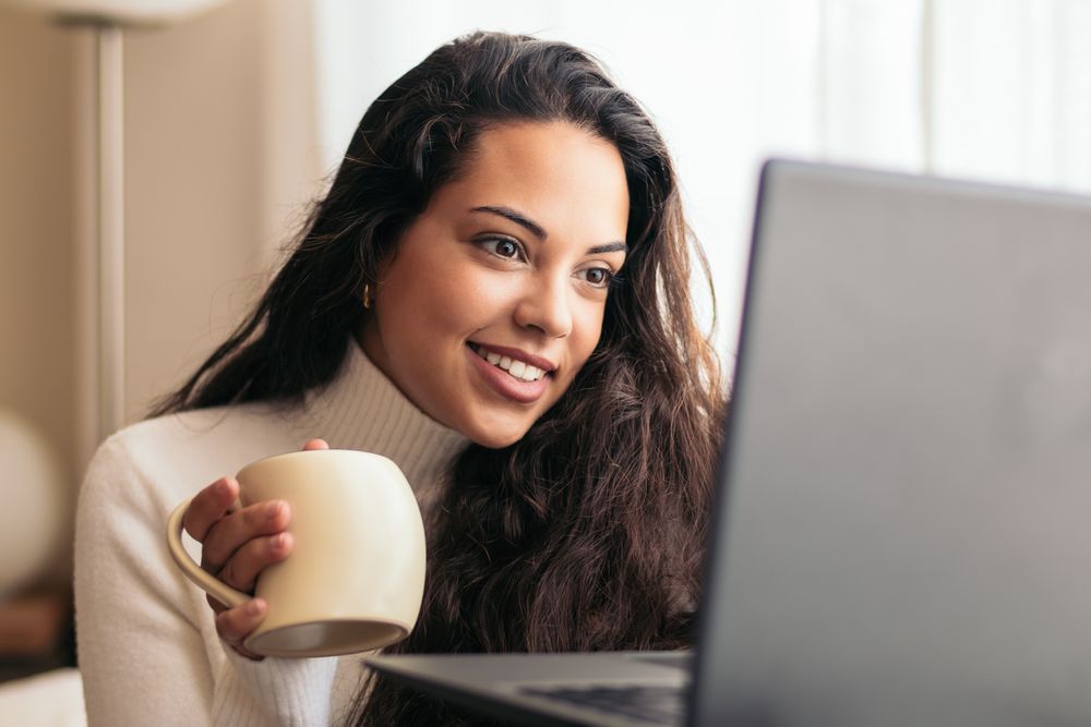 Young Woman Enjoying a Cup of Coffee While Using Laptop