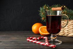 Glass of tasty mulled wine on decorated wooden background, space for text
