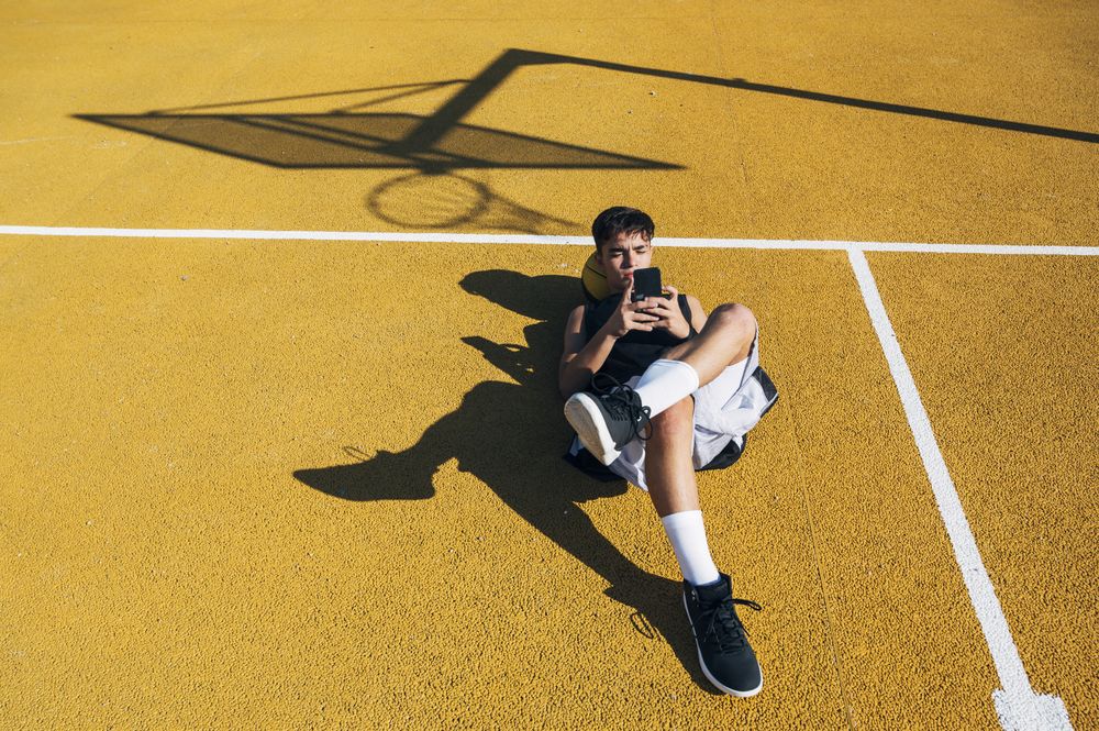 Male basketball player using his smartphone resting after training