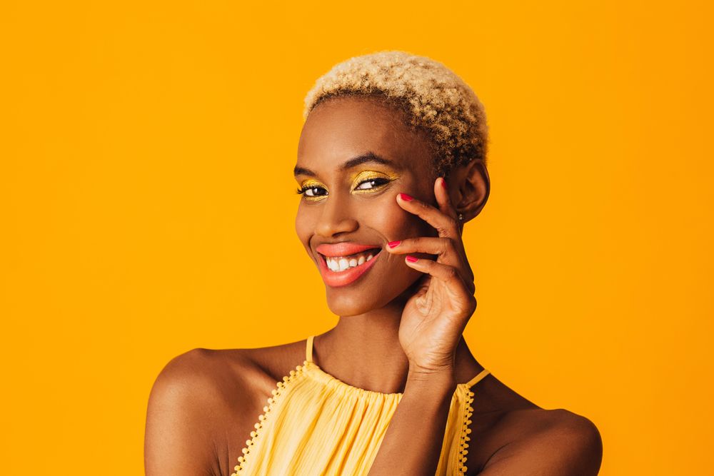 Black woman with short blonde hair looking at camera with hand to cheek
