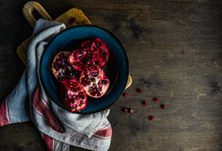 Top view of ceramic bowl of open pomegranates on wooden table
