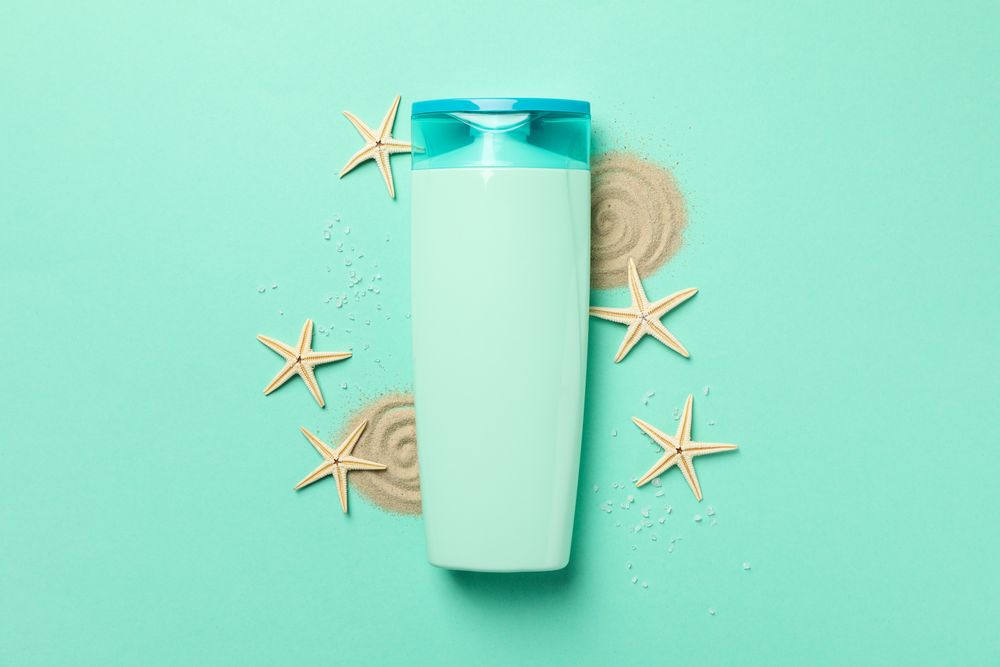 Bottle of shampoo, starfishes and sand on mint background