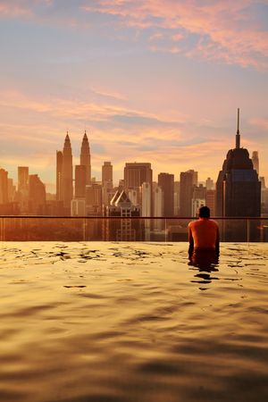 Man relax in swimming pool in sunrise, enjoying city view in the morning