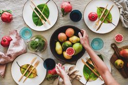 Fresh table setting with leaves on bright plates, glassware, with person reaching for fruit bowl
