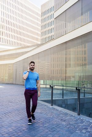 Portrait of cheerful modern businessman speaking on phone while walking outdoors