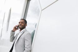 Elegant Black man talking smartphone leaning on geometrical wall