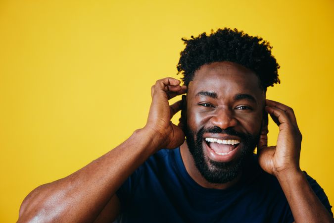 Portrait of joyful Black man with both hands to his head on yellow background