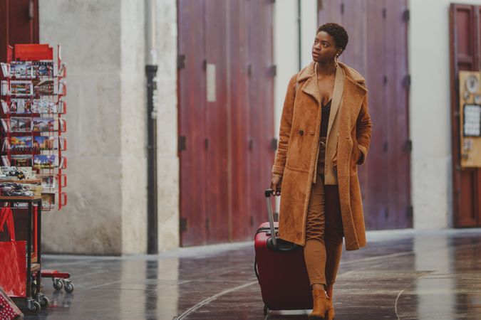 Stylish Black woman with luggage walking on street