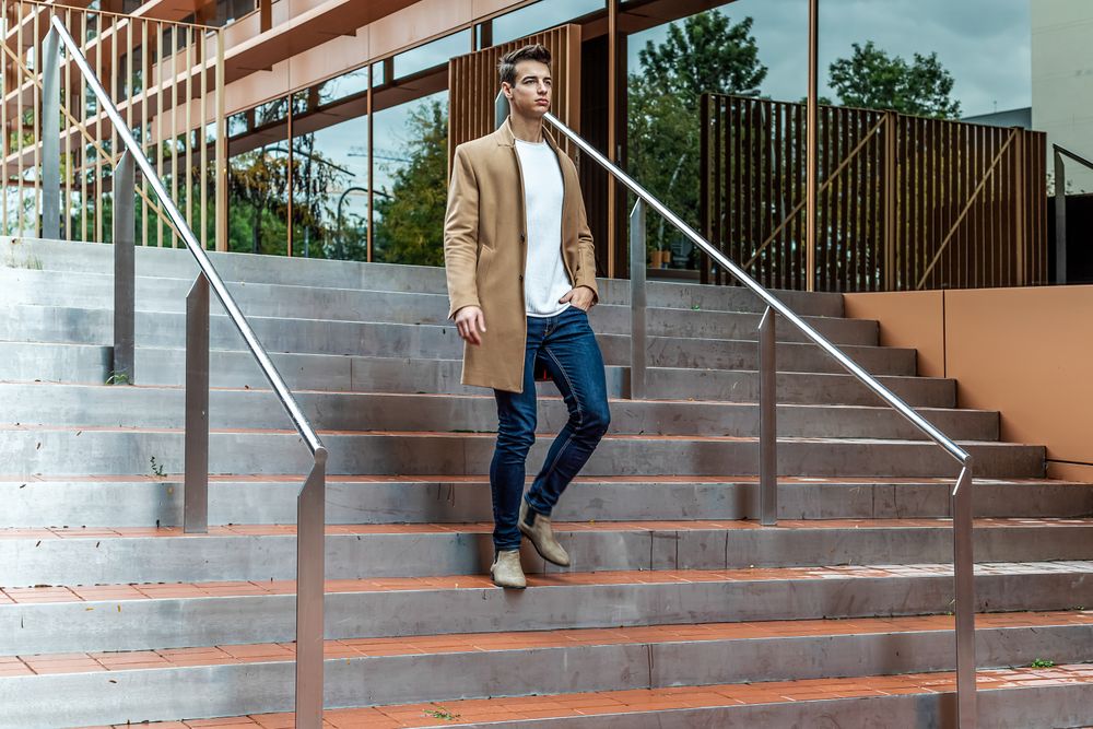 Male in camel coat walking down staircase outside