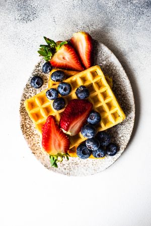 Top view of waffle breakfast with blueberries & strawberries served on grey counter