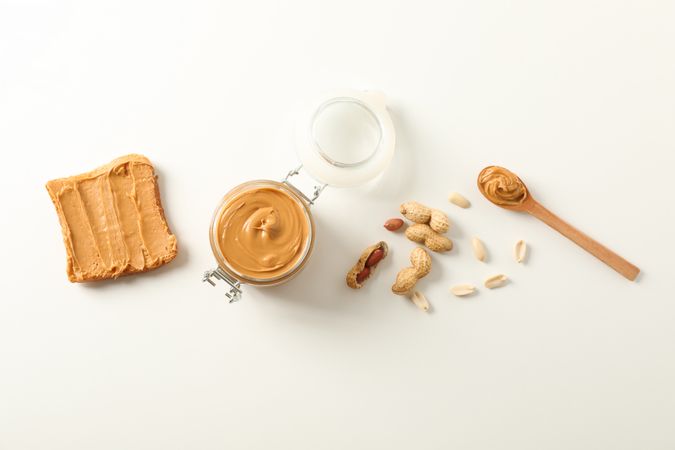 Flat lay composition with peanut butter sandwich, glass jar, peanut and spoon on light background, space for text