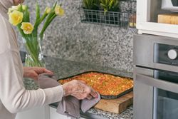 Crop mature woman baking pizza at home