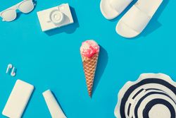 Summer objects of flip flops, sunglasses, camera, smart phone, hat and ice cream on blue background