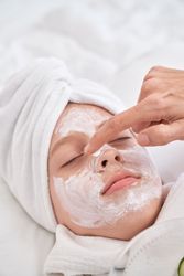 Woman applying cream mask on face of child
