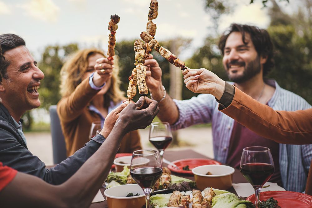 Group of happy people at bbq lifting up their kebab skewers