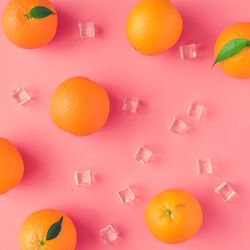 Whole oranges, and ice cubes on vivid pink background