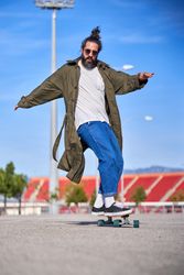 Stylish hipster male riding skateboard in city park
