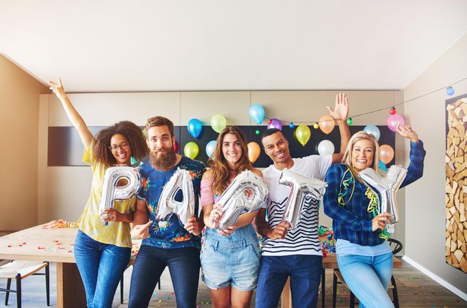 Happy friends with their arms up with silver balloons saying “Party”