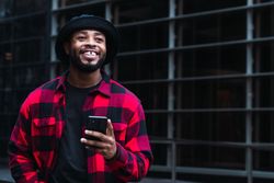 Cheerful Black male with smartphone in contemporary building