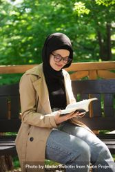 Woman in headscarf calmly reading in a wooded park bYXM14