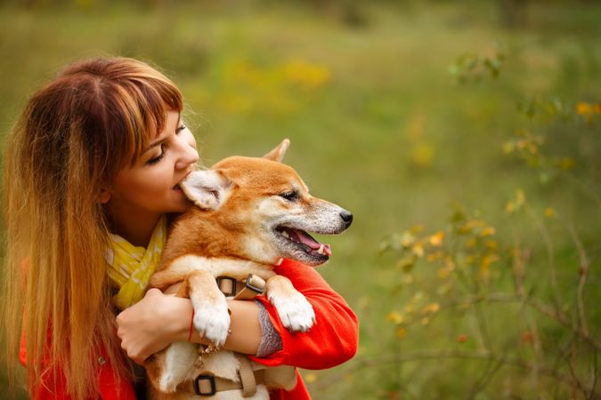 Female in red coat holding her shibu dog standing in field