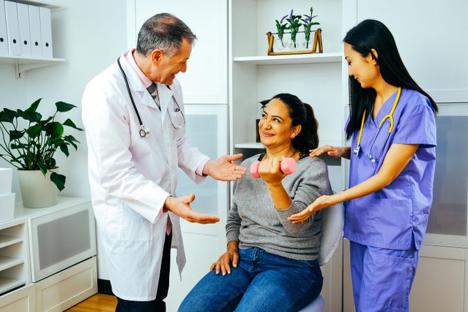 Amusing doctor and physiotherapist helping patient with arm rehab exercises