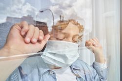 Child in medical mask standing near window