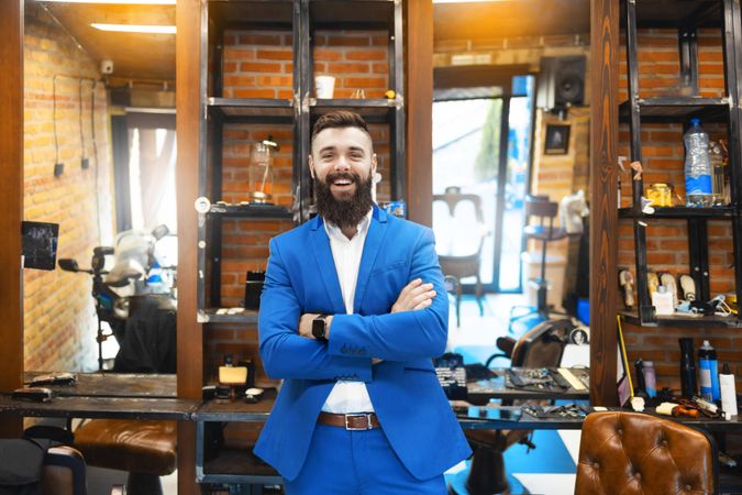 Man in sharp blue suit with arms crossed smiling in barbershop