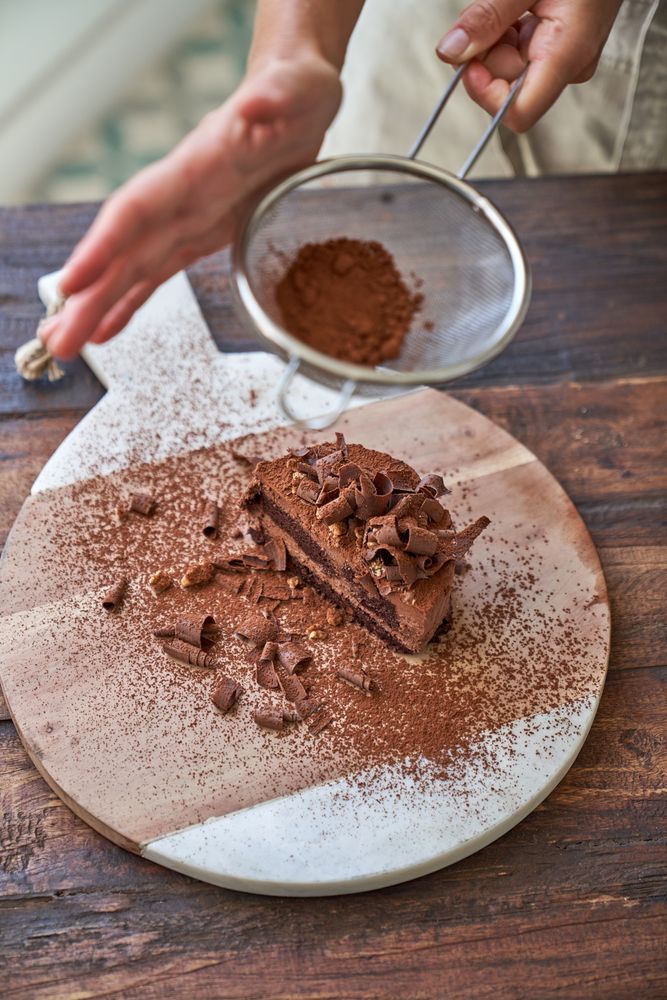 Crop woman preparing chocolate cake with cocoa powder