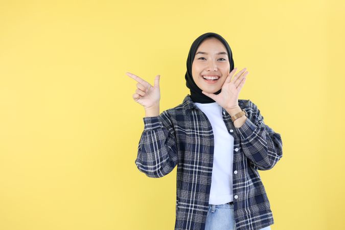 Happy Indonesian Young Woman in Veil or Hijab, Pointing at Copy Space with Right Hand