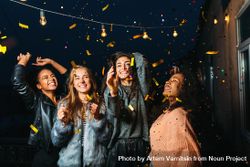 Group of female friends throwing confetti at night bed6K4