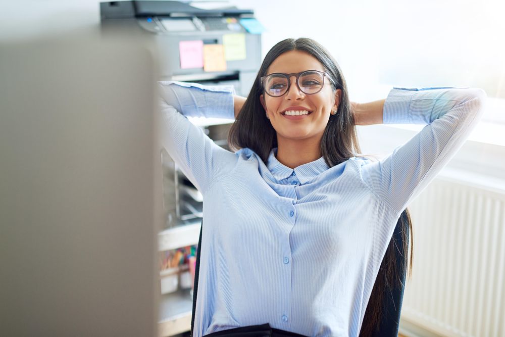 Smiling female sitting at her desk relaxing with her hands behind her head