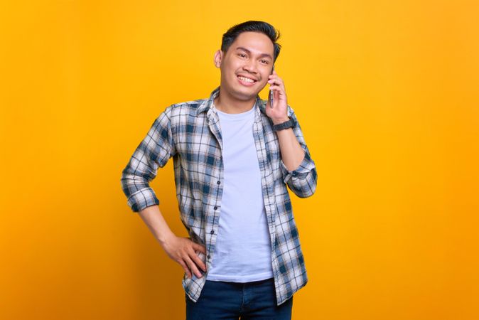 Confident Asian male talking on phone in studio shoot with hand on his hip