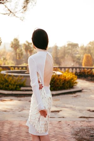 Woman looking out at view standing on brick patio in white formal dress