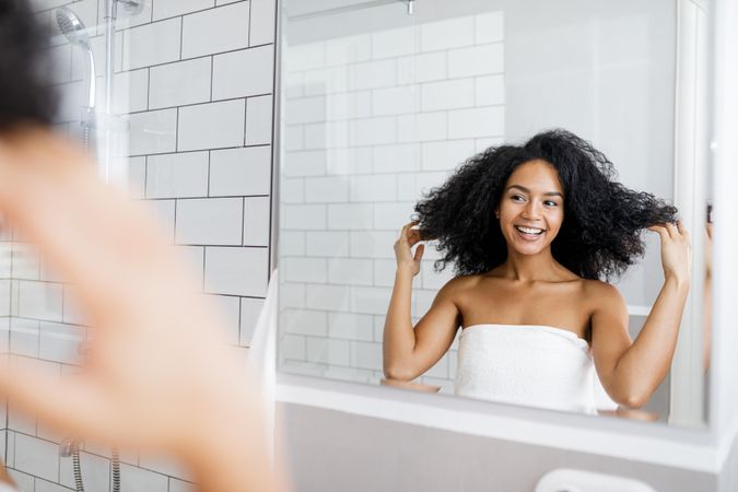 Happy Black woman standing in bathroom, holding her curly hair