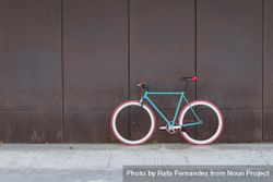 Red and green bicycle parked against a brown wall, copy space 5zxWPb