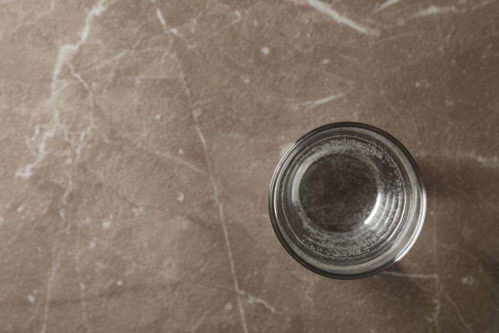 Looking down at single water glass on grey marble table