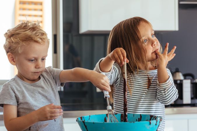 Little boy and girl mixing batter in a bowl for baking, with girl licking her fingers