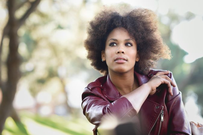 Calm woman sitting outside in red leather jacket looking in the distance