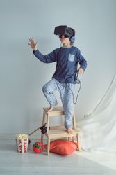 Boy in VR goggles and headphones standing on stool stepladder