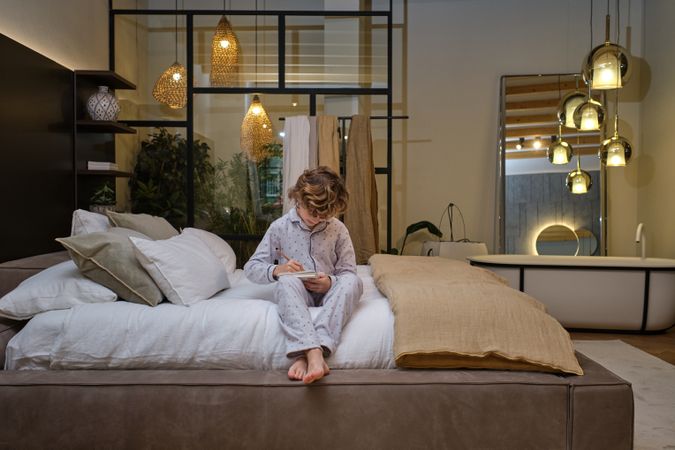 Concentrated boy writing in notepad on bed