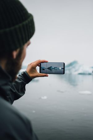 Man taking picture of glacier with smart phone, vertical