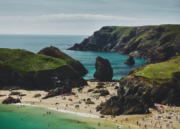Busy beach in Cornwall surrounded by green cliffs