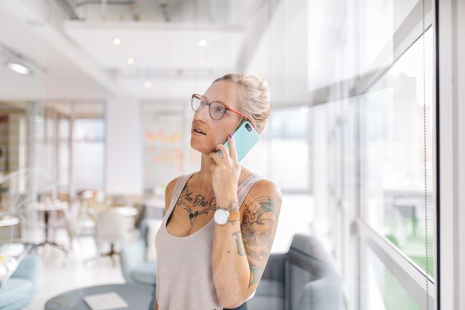 Tattooed woman speaking on a mobile phone in a bright modern office