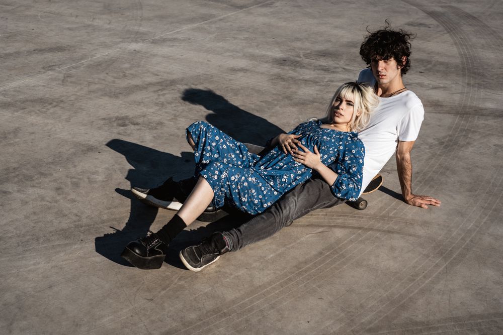 Trendy couple sitting together on skateboard on street